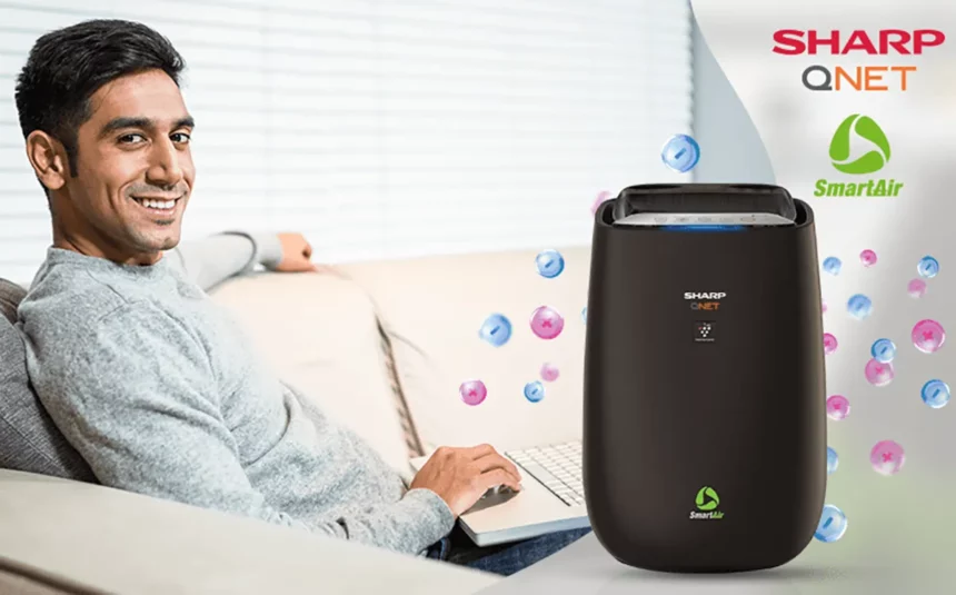 A happy Indian man working with his laptop on the sofa with SHARP QNET SmartAir in the frame