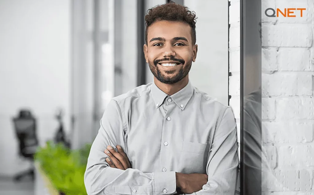 A young man smiling with confidence and standing with his arm crossed