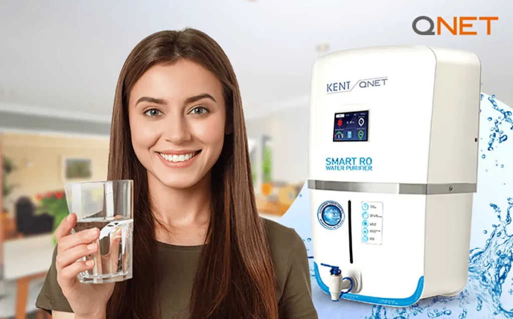 A young Woman holding a galss of water with KENT QNET RO Water Putrifier in background